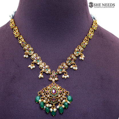 Close-up of ornate royal necklace pendant with green emerald-style stones, ruby accents, white stones and multiple pearl and green bead drops|She Needs Jewellery

