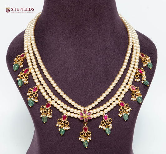 Royal gold layered pearl necklace featuring pink and green stone charms, floral centerpiece, pearl strands, and gold-plated detailing.|She Needs Jewellery
