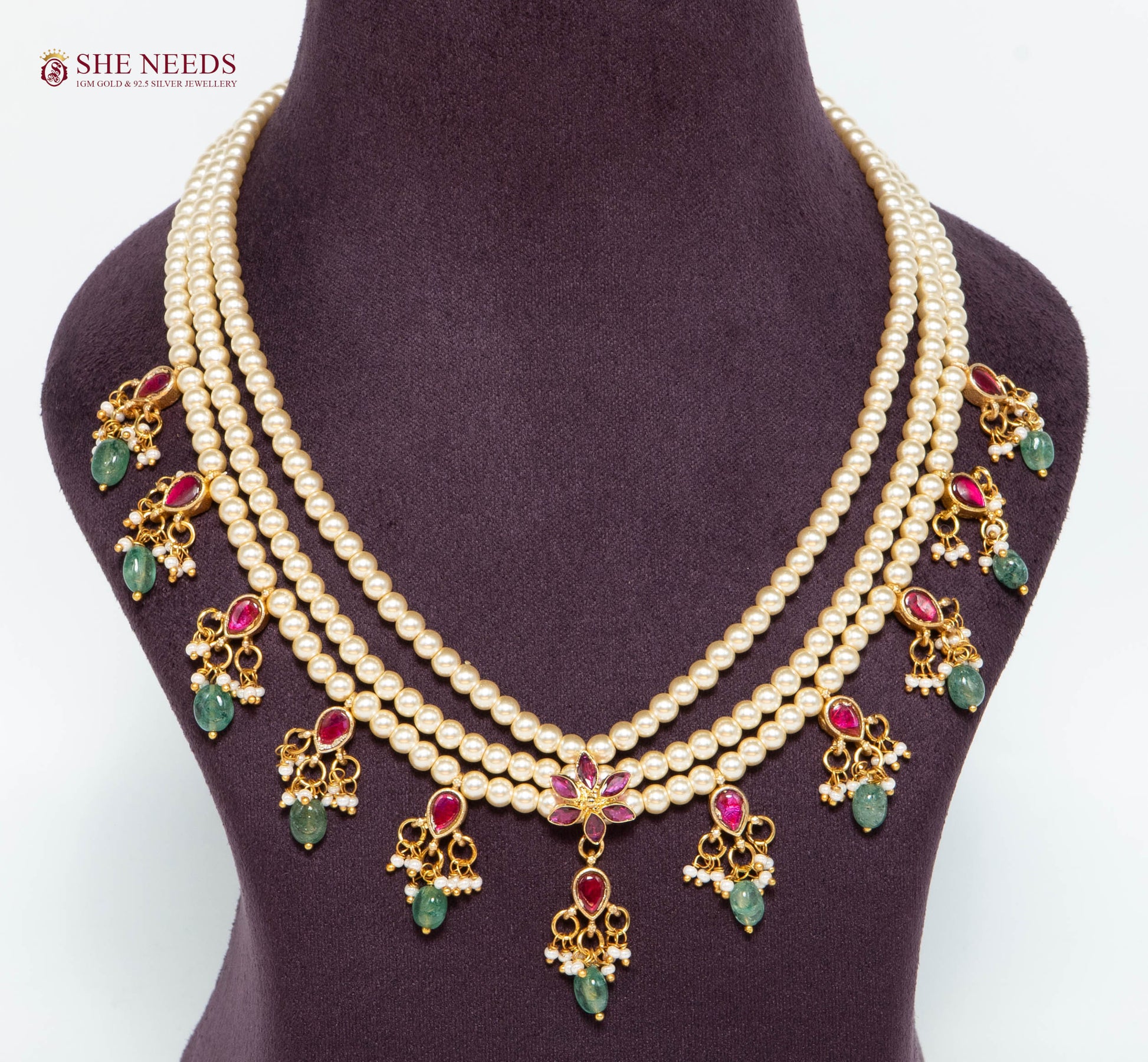 Royal gold layered pearl necklace featuring pink and green stone charms, floral centerpiece, pearl strands, and gold-plated detailing.|She Needs Jewellery
