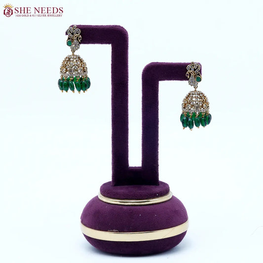 Antique gold jhumka earrings featuring crystal-studded peacock motifs, sparkling CZ stones, intricate dome detailing, and rich green bead drops.|She Needs Jewellery
