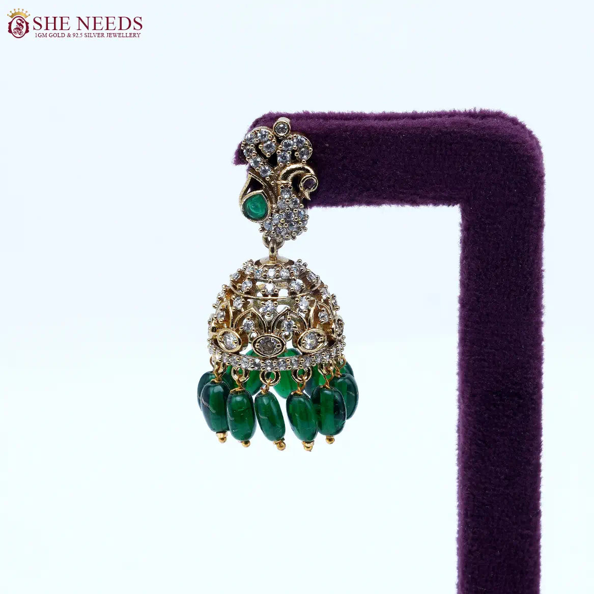 Antique gold jhumka earrings featuring crystal-studded peacock motifs, sparkling CZ stones, intricate dome detailing, and rich green bead drops.|She Needs Jewellery
