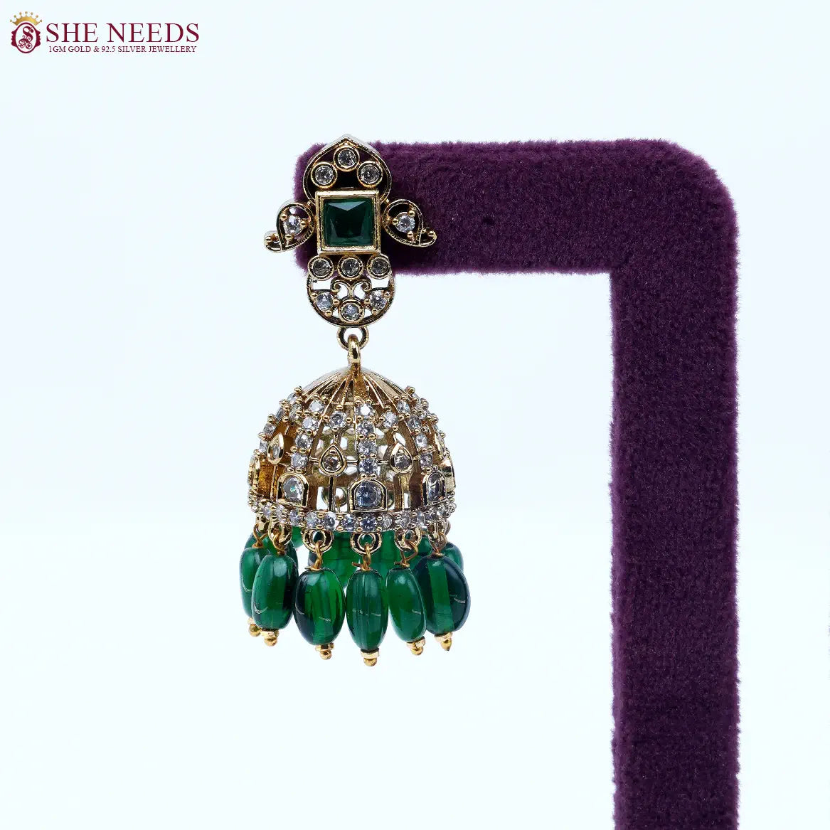 Gold-tone dome jhumka earrings featuring sparkling white stones, emerald green square stud accents, and dark green bead drops in a traditional ethnic design.|She Needs Jewellery
