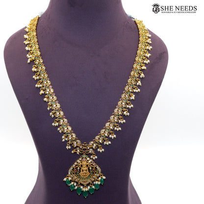 Long gold-toned Lakshmi necklace featuring intricate temple motifs, emerald green stones, ruby accents, white stones and pearl drops|She Needs Jewellery
