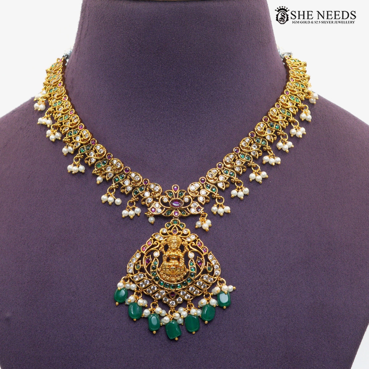 Close-up of ornate Lakshmi necklace pendant with traditional goddess motif, emerald green stones, ruby accents, white stones and pearl drops|She Needs Jewellery
