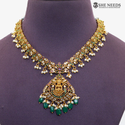 Close-up of ornate Lakshmi necklace pendant with traditional goddess motif, emerald green stones, ruby accents, white stones and pearl drops|She Needs Jewellery
