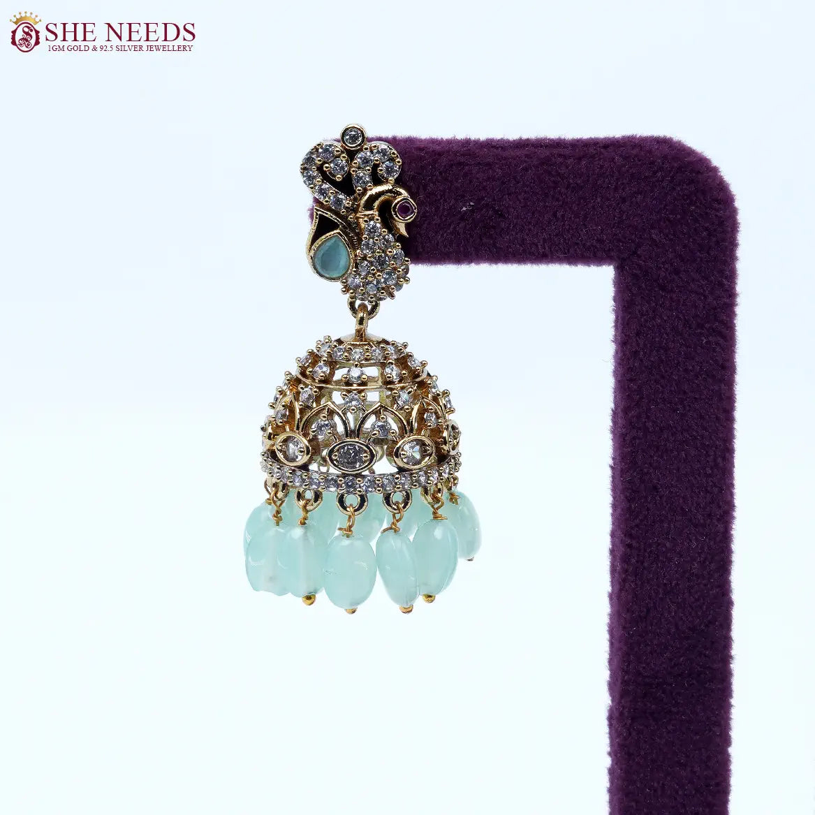 Antique gold jhumka earrings featuring crystal-studded peacock motifs, sparkling CZ stones, intricate dome detailing, and elegant light green bead drops. |She Needs Jewellery