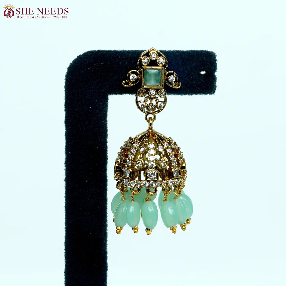 Gold-tone dome jhumka earrings featuring crystal embellishments, light green square stones, and light green bead drops in an elegant traditional design. |She Needs Jewellery

