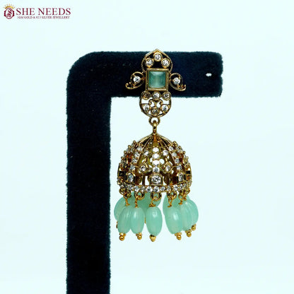 Gold-tone dome jhumka earrings featuring crystal embellishments, light green square stones, and light green bead drops in an elegant traditional design. |She Needs Jewellery
