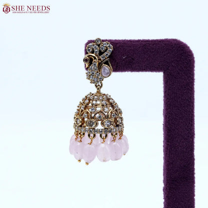 Antique gold jhumka earrings featuring crystal-studded peacock motifs, sparkling CZ stones, intricate dome detailing, and soft light pink bead drops. |She Needs Jewellery