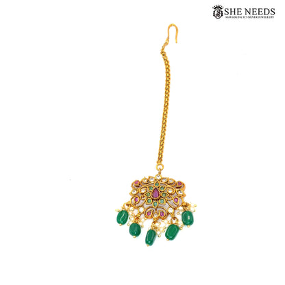 Gold-plated traditional maang tikka with intricate peacock-inspired stonework, green emerald-style beads, ruby accents, white stones and pearl embellishments|She Needs Jewellery

