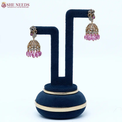 Antique gold jhumka earrings featuring crystal-studded peacock motifs, sparkling CZ stones, intricate dome detailing, and vibrant pink bead drops.| She Needs Jewellery