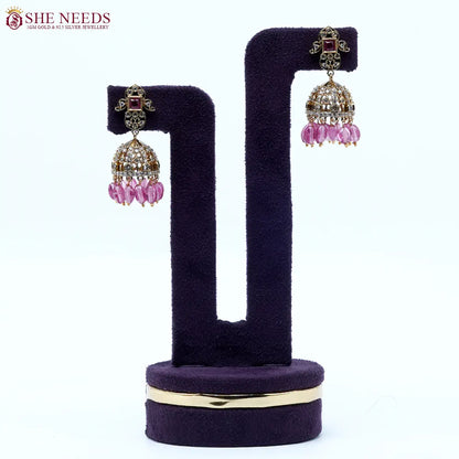 Gold-tone dome jhumka earrings adorned with white stones, rose pink square stud accents, and translucent pink bead drops, perfect for festive and party wear.|She Needs Jewellery
