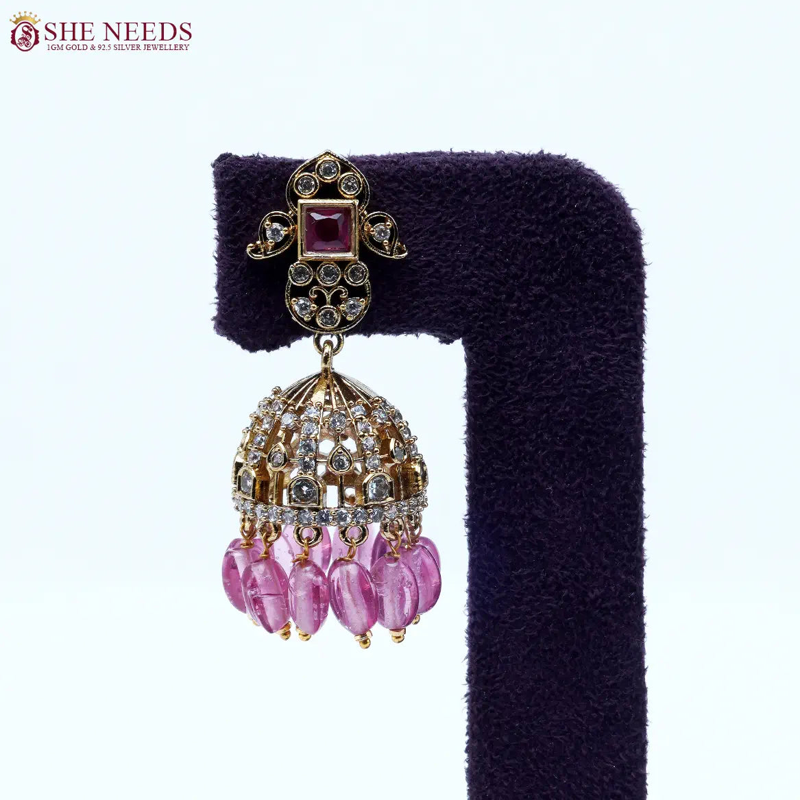 Gold-tone dome jhumka earrings adorned with white stones, rose pink square stud accents, and translucent pink bead drops, perfect for festive and party wear.|She Needs Jewellery
