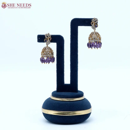 Antique gold jhumka earrings featuring crystal-studded peacock motifs, sparkling CZ stones, intricate dome detailing, and royal purple bead drops.|She Needs Jewellery
