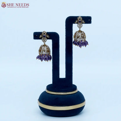 Gold-tone dome jhumka earrings featuring dazzling white stones, amethyst purple square stone accents, and rich purple bead drops in a luxurious ethnic style |She Needs Jewellery
