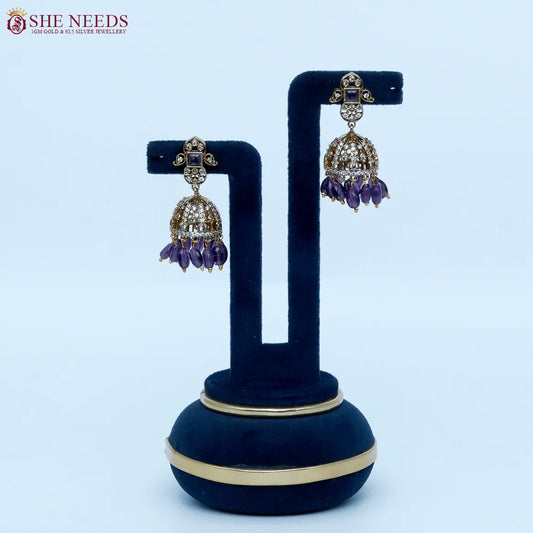 Gold-tone dome jhumka earrings featuring dazzling white stones, amethyst purple square stone accents, and rich purple bead drops in a luxurious ethnic style |She Needs Jewellery
