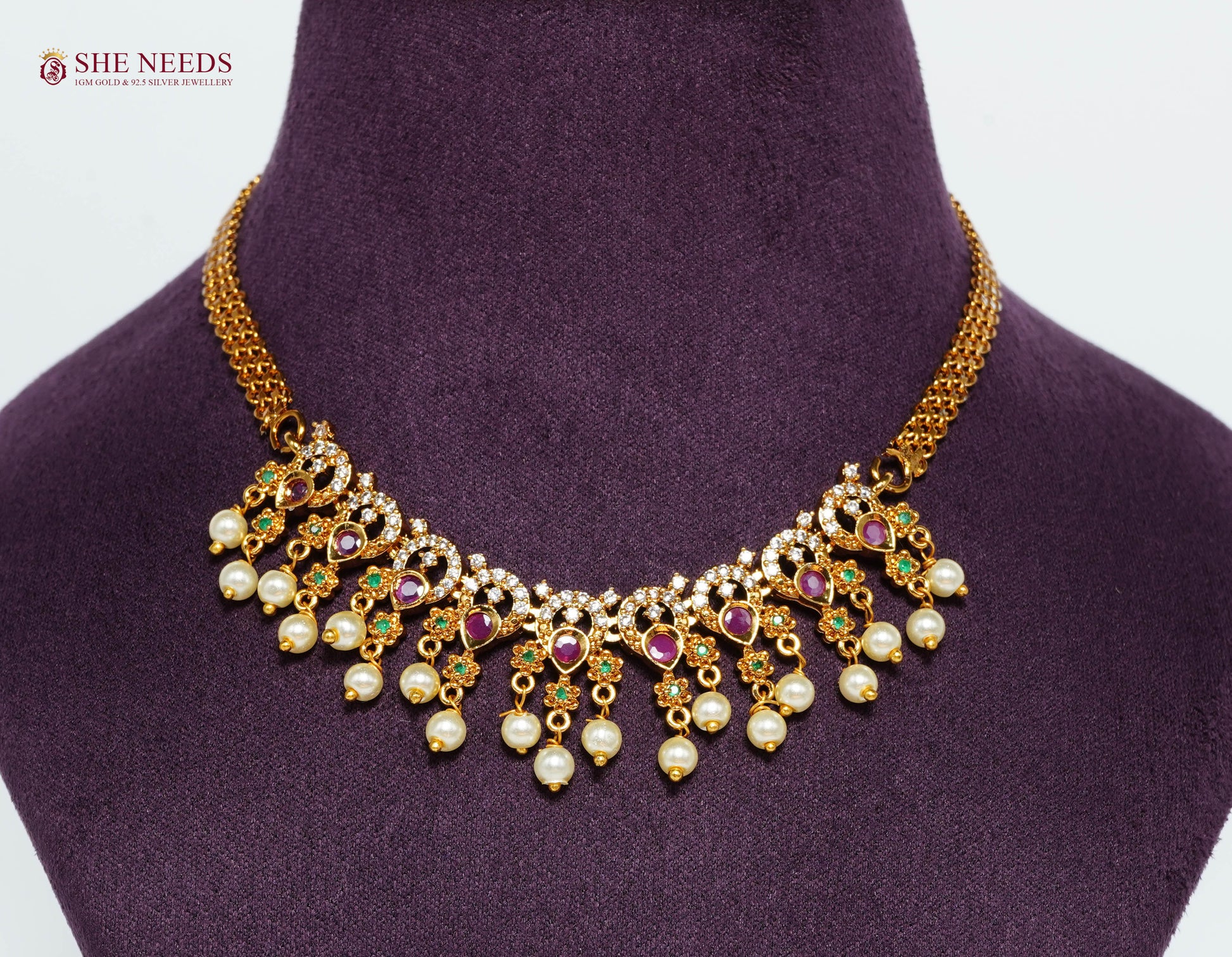 Close-up of a gold-plated royal ruby pearl fringe necklace featuring American Diamonds, emerald accents, and pearl drop detailing.|She Needs Jewellery
