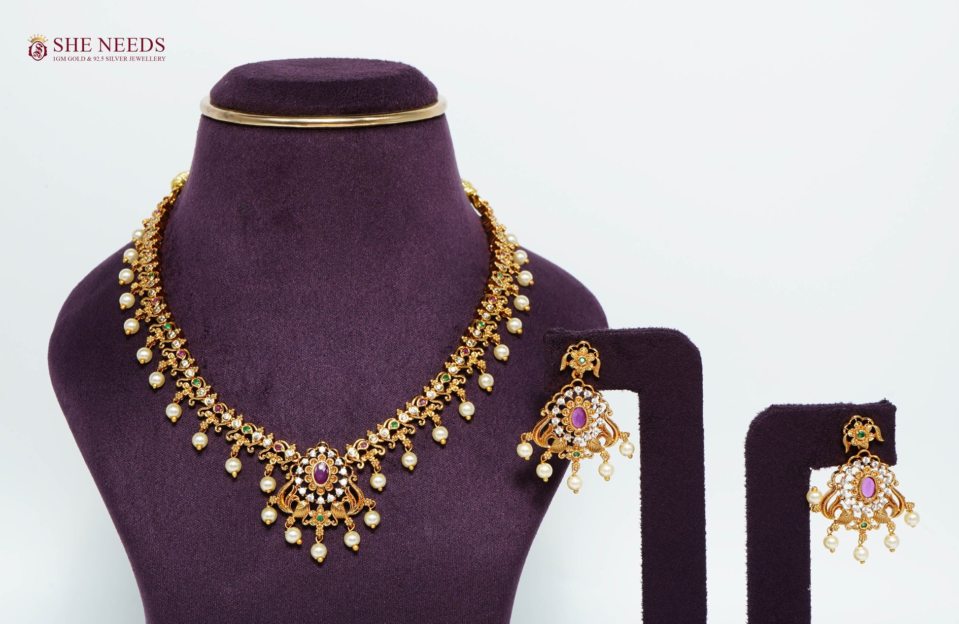 Gold-plated Royal Ruby Pearl Peacock Necklace Set featuring ruby stones, American diamonds, pearl drops, peacock motifs, and matching statement earrings for bridal and festive wear.|She Needs Jewellery
