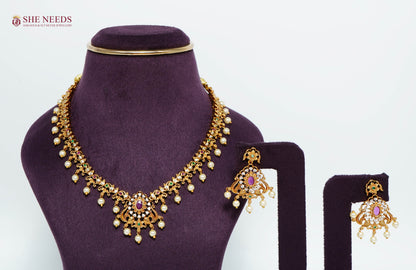 Gold-plated Royal Ruby Pearl Peacock Necklace Set featuring ruby stones, American diamonds, pearl drops, peacock motifs, and matching statement earrings for bridal and festive wear.|She Needs Jewellery
