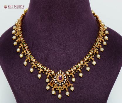 Gold-plated peacock necklace featuring ruby stones, American diamonds, intricate floral detailing, and elegant pearl drops.|She Needs Jewellery
