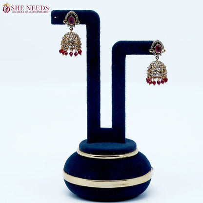 Royal Stone Antique Ruby Jhumka Earrings featuring sparkling American Diamonds, antique gold detailing, ruby stone centerpiece, and ruby crystal bead drops.|She Needs Jewellery

