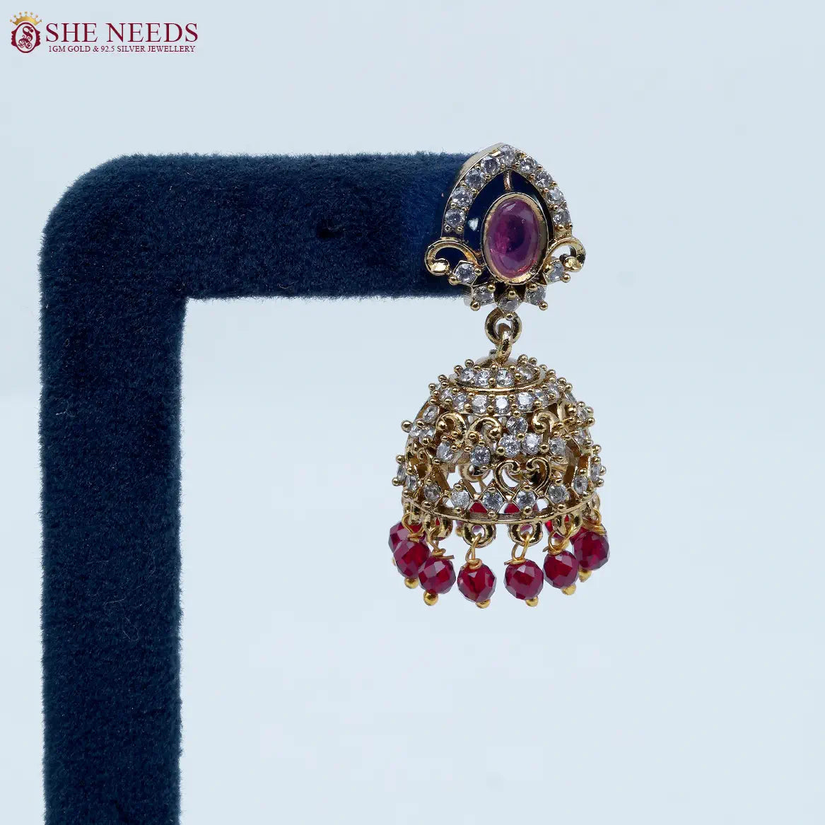 Royal Stone Antique Ruby Jhumka Earrings featuring sparkling American Diamonds, antique gold detailing, ruby stone centerpiece, and ruby crystal bead drops.|She Needs Jewellery
