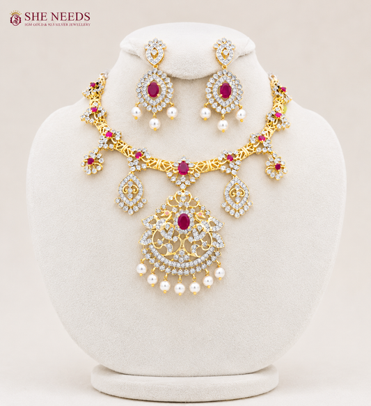 Elegant ruby pink AD stone bridal necklace set with pearl drop earrings in premium gold finish displayed on white mannequin.