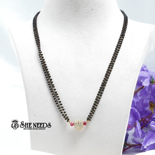 Ruby red dual-string mangalsutra with black beads, CZ-studded spherical pendant, red bead accents, and gold-tone finish displayed on a white jewelry bust |She Needs Jewellery
