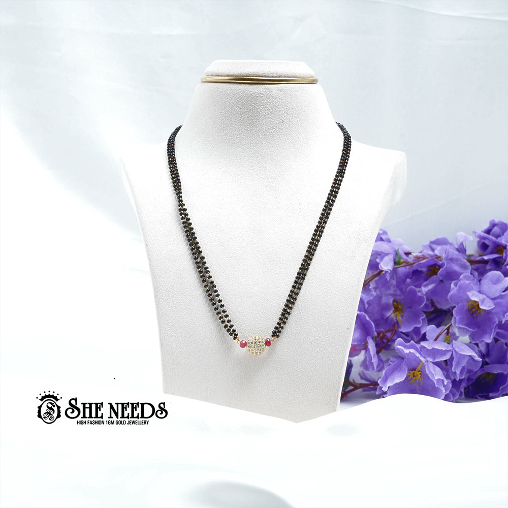 Ruby red dual-string mangalsutra with black beads, CZ-studded spherical pendant, red bead accents, and gold-tone finish displayed on a white jewelry bust |She Needs Jewellery
