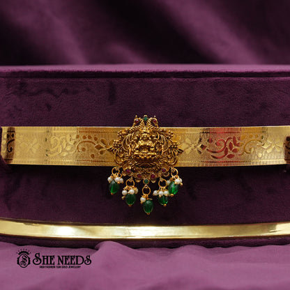 Traditional gold-finish kids vaddanam featuring a central Sri Lakshmi motif, intricate temple engravings, pearl accents, and elegant green bead drops.|She Needs Jewellery

