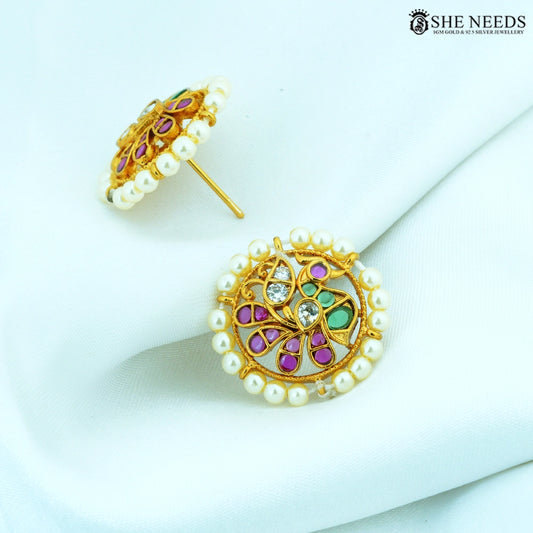 Angled view of Vamika Antique Gold Pearl Floral Stud Earrings showcasing pearl border, floral swirl design, ruby-colored stones, emerald-colored stones and American Diamonds.|She Needs Jewellery
